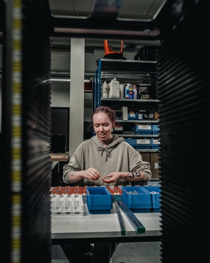 Lachende medewerker bij een werkbank met onderdelen.